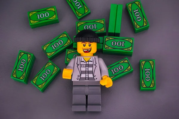 Lego criminoso com tijolos de dinheiro Lego em fundo cinza . — Fotografia de Stock