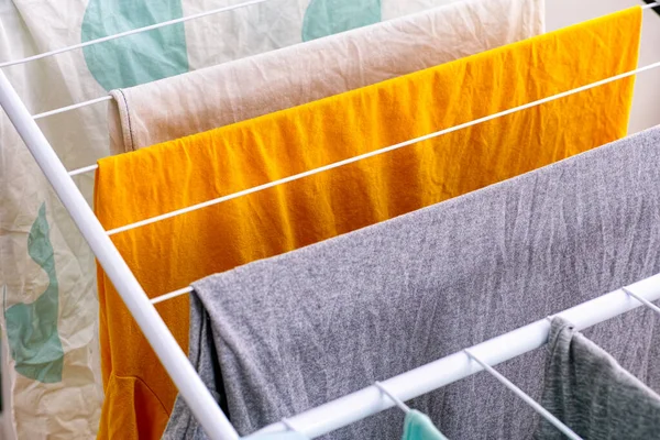 Washed laundry hanging on clothing dryer rack indoor. Closeup.