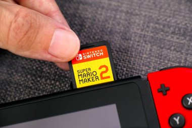 Tambov, Rusya Federasyonu - 9 Temmuz 2019 Erkek parmakları Nintendo Oyun Konsoluna Super Mario Maker 2 video oyunu kartuşu yerleştiriyor.