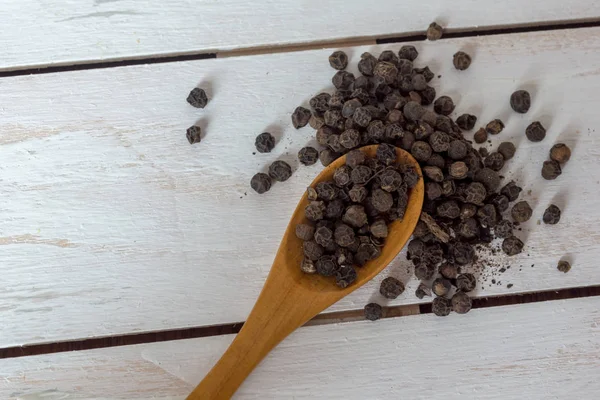 Closeup view of black pepper corns and spoon — Stock Photo, Image