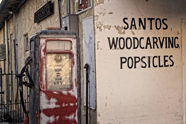 一座古老的西方建筑 在破旧的老式气体泵旁推广圣人 Woodcrvings 和冰棒 — 图库照片