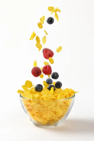 Fruits à baies et flocons de maïs tombant dans le bol — Photo