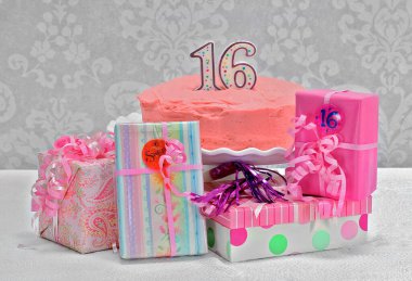   Pembe 16 yaş günü pastası içinde hediyelerle çevrili. Pastaya ve mumlara odaklan.