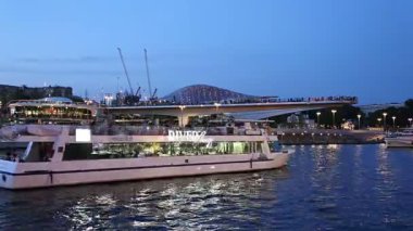 MOSCOW, RUSSIA - AUGUST  11, 2019: Floating bridge of Zaryadye park on Moskvoretskaya Embankment of Moskva River (and tourist pleasure boat) at Night. Moscow, Russia. 