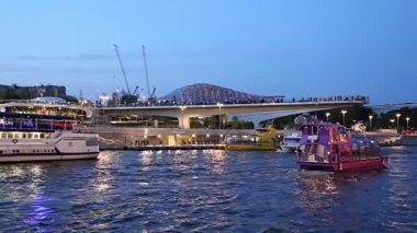 MOSCOW, RUSSIA - AUGUST  11, 2019: Floating bridge of Zaryadye park on Moskvoretskaya Embankment of Moskva River (and tourist pleasure boat) at Night. Moscow, Russia. 