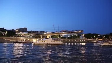 MOSCOW, RUSSIA - AUGUST  11, 2019: Floating bridge of Zaryadye park on Moskvoretskaya Embankment of Moskva River (and tourist pleasure boat) at Night. Moscow, Russia. 