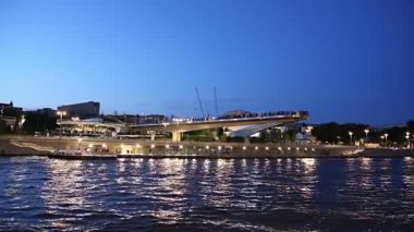 MOSCOW, RUSSIA - AUGUST  11, 2019: Floating bridge of Zaryadye park on Moskvoretskaya Embankment of Moskva River (and tourist pleasure boat) at Night. Moscow, Russia. 