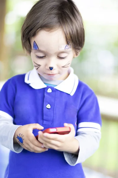 Piękny Chłopiec Malowaną Twarzą Gra Telefonie Komórkowym — Zdjęcie stockowe