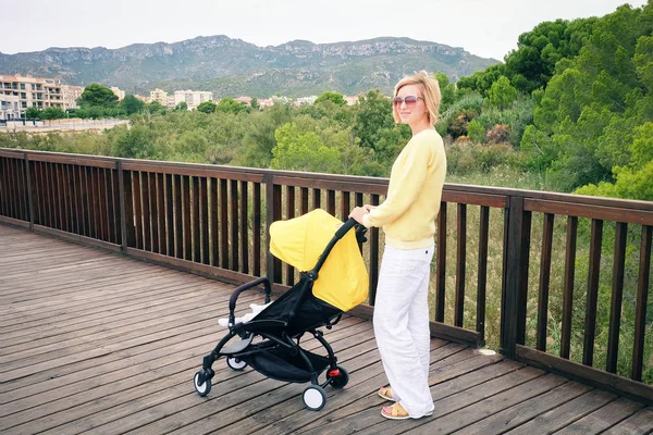 Capelli biondi donna passeggiando un bambino in carrozza — Foto Stock