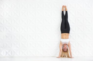 Young blonde woman doing a handstand over a white wall clipart