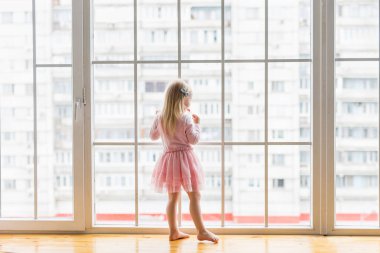 Mutlu küçük kız pencerenin önünde dururken gülümsüyor.