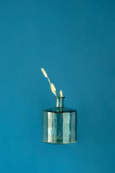 Florero de vidrio turquesa con flor de hierba seca para la decoración de interiores en la pared azul — Foto de Stock