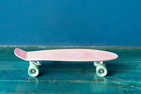 Skateboard rosa sul pavimento in legno contro la parete blu — Foto Stock