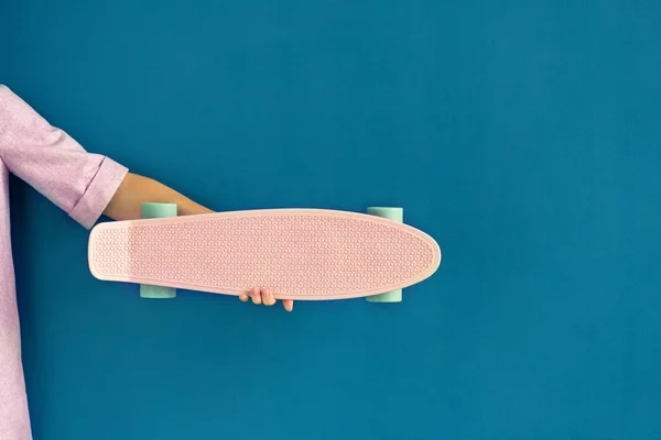 Femme tenant skateboard rose contre mur bleu — Photo