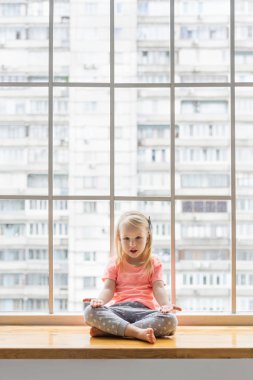 3,5 yaşında bir kız pencerenin önünde yoga yapıyor.