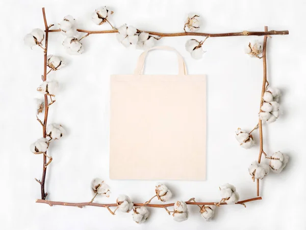 Colocação plana de saco de tecido em branco com ramos de flor de algodão no fundo branco — Fotografia de Stock