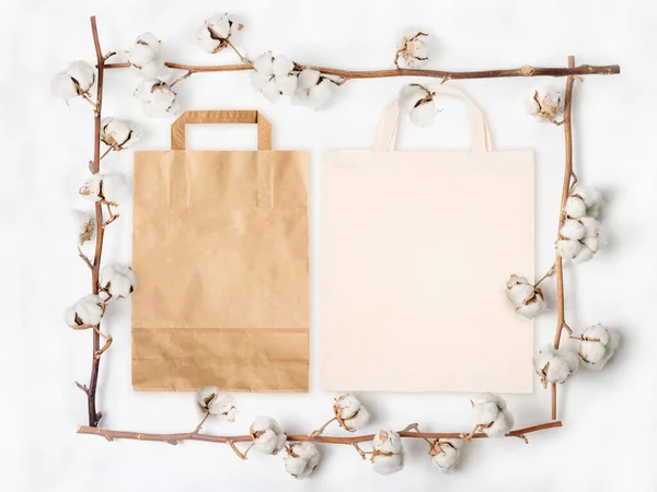 Papiertüte und Baumwolltasche im Rahmen aus Baumwollblumenzweigen auf weißem Hintergrund — Stockfoto