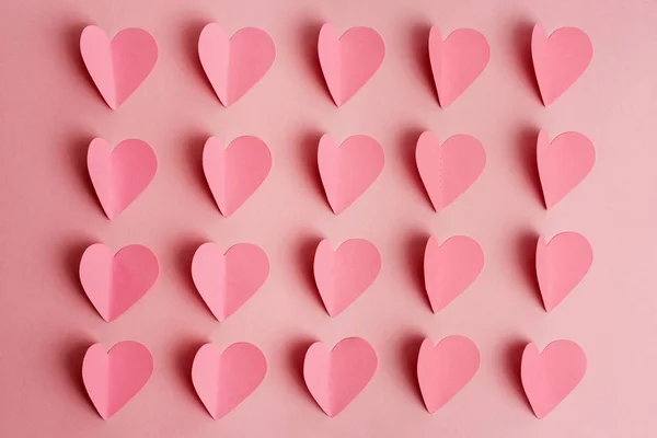 Corações de papel rosa no fundo rosa. Corações de papel dispostos em fileiras no fundo rosa. Depósito plano — Fotografia de Stock