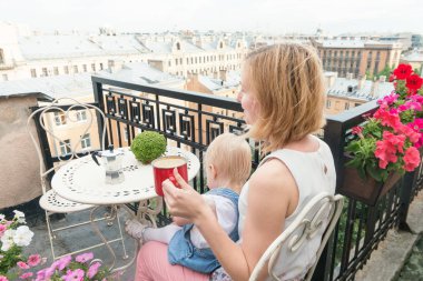 Annem bir bebekle balkonda otururken kahve molası veriyor.