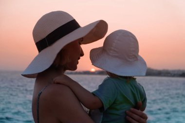 Genç anne gün batımında küçük kızına sarılıyor.