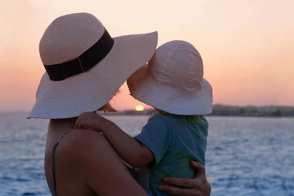 母は赤ん坊を抱きかかえながら夕日の海を見ている — ストック写真