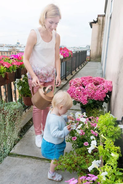 Giovane madre con il suo bambino baia ragazza irrigazione fiori — Foto Stock