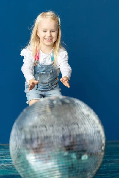 Happy toddler blonde girl havig fun while rolling giant disco ball on the floor — Stock Photo, Image