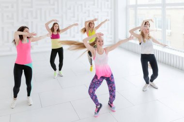 Young women in sportswear dancing with hands raised up at dance fitness class