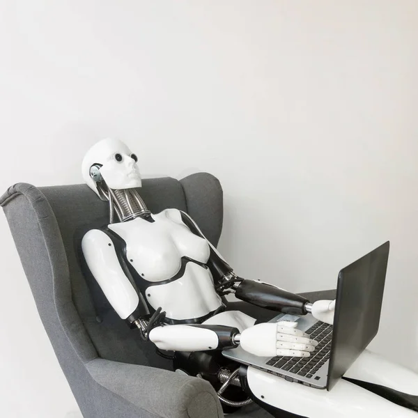 Closeup of white plastic robot working with laptop while sitting in armchair — Stok fotoğraf