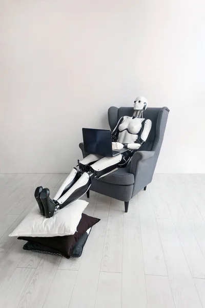 Robot trabajando con el ordenador portátil mientras está sentado en un acogedor sillón en la habitación blanca — Foto de Stock