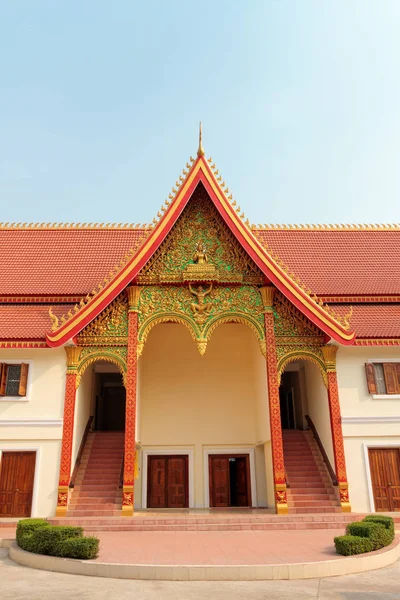 An entrance of Buddhist temple with ornate red roof in Vientiane in Laos against blue sky — Stok fotoğraf