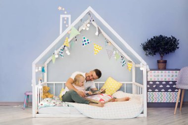 Happy father dad in cute house bed with blonde daughter reading stories at bedtime