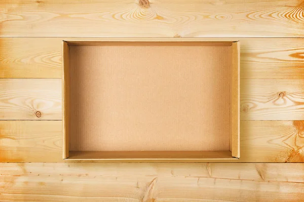 木製の背景に段ボール箱を開きます。天然木の質感に空の段ボールパッケージ — ストック写真