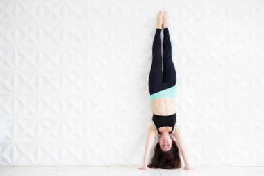 Genç esmer kadın beyaz bir duvarın üzerinde amuda kalkıyor.