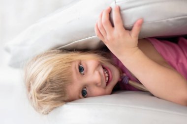 Küçük mutlu kız yatakta yastıklarla oynarken gülümsüyor.