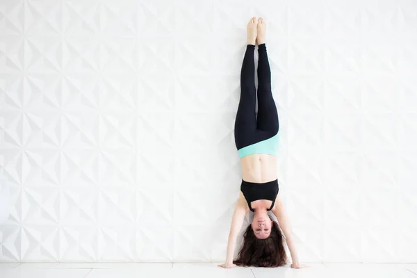 Wanita muda berambut cokelat melakukan handstand atas dinding putih — Stok Foto