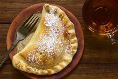 Krema şeker, yan, çay ile Şili elma empanada ek yükü doğal ışık ile karanlık ahşap üzerine fotoğraflandı.