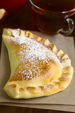 Doğal ışık (seçici odak, odak üçte biri haline empanada ile koyu ahşap üzerine krema şeker, çay arkada ile Şili elma empanada fotoğrafı)