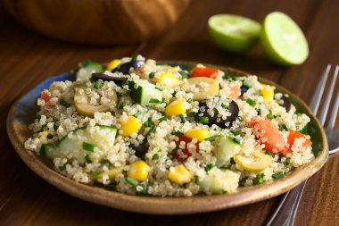 Quinoa salata tatlı mısır, zeytin, domates, salatalık ve plaka üzerinde koyu renkli ahşap doğal ışık (seçici odak, odak ortasında salata ile fotoğraflandı, chives ile)