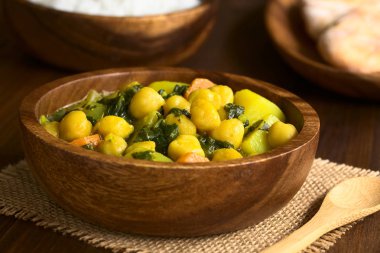 Vegan nohut köri veya doğal ışık (seçici odak, odak üçte biri haline köri ile fotoğraflandı ahşap kase, chana masala ıspanak, patates ve havuç ile hizmet)