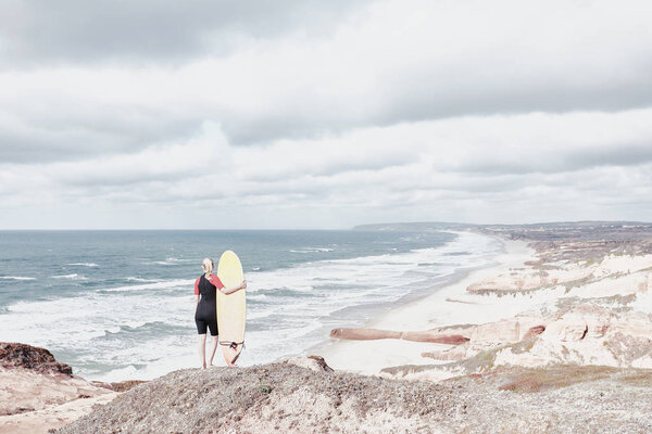 Surfer girl on cliff near ocean