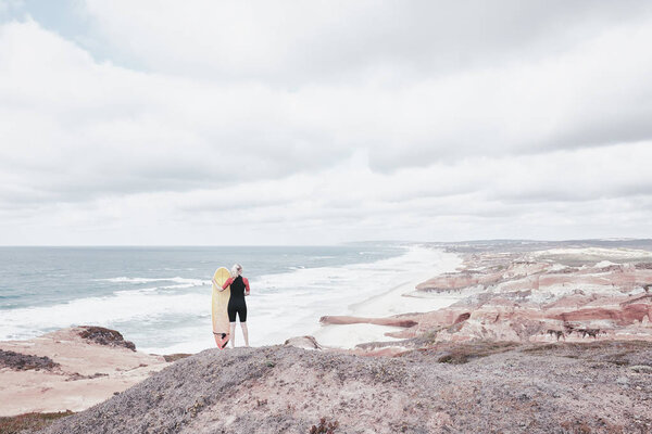 Surfer girl on cliff near ocean