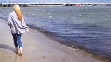 Genç bir kadın sahilde yürüyor.