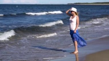 Genç bir kadın sahilde yürüyor.