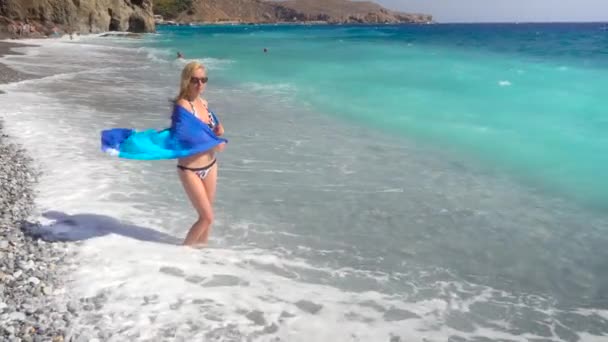 Молодая женщина прогуливается по пляжу с синим морем — стоковое видео