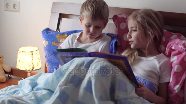 Милі діти читають книгу в ліжку — стокове відео