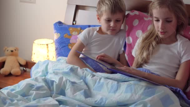 Niedliche Kinder lesen Buch im Bett — Stockvideo