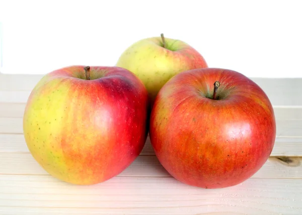 Three ripe red apples in beige wooden shelf closeup — Stock Photo, Image