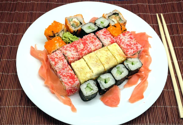 Sushi na bílé plotně s hůlkami nad proutěný slaměné mat closeup — Stock fotografie