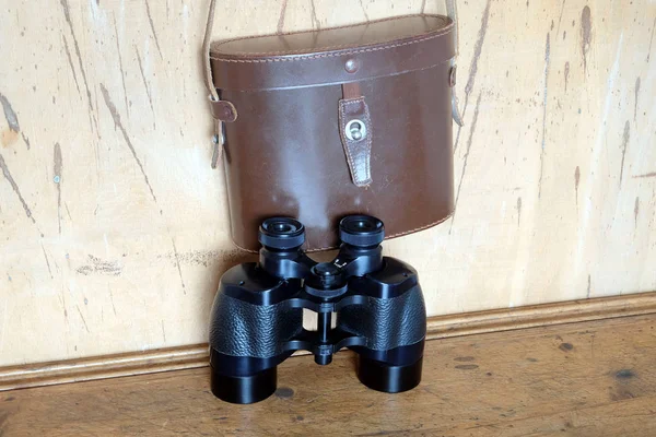 Vintage prism black color binoculars and brown leather case on the wall